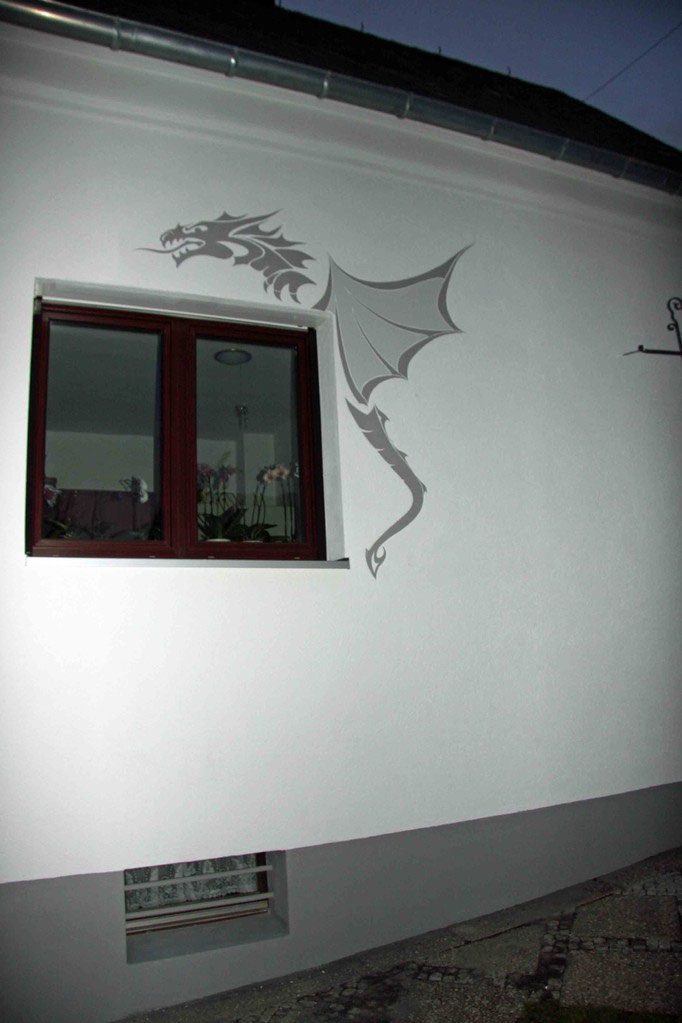 Weiße Hausfassade mit aufgemaltem Drachen neben einem Fenster