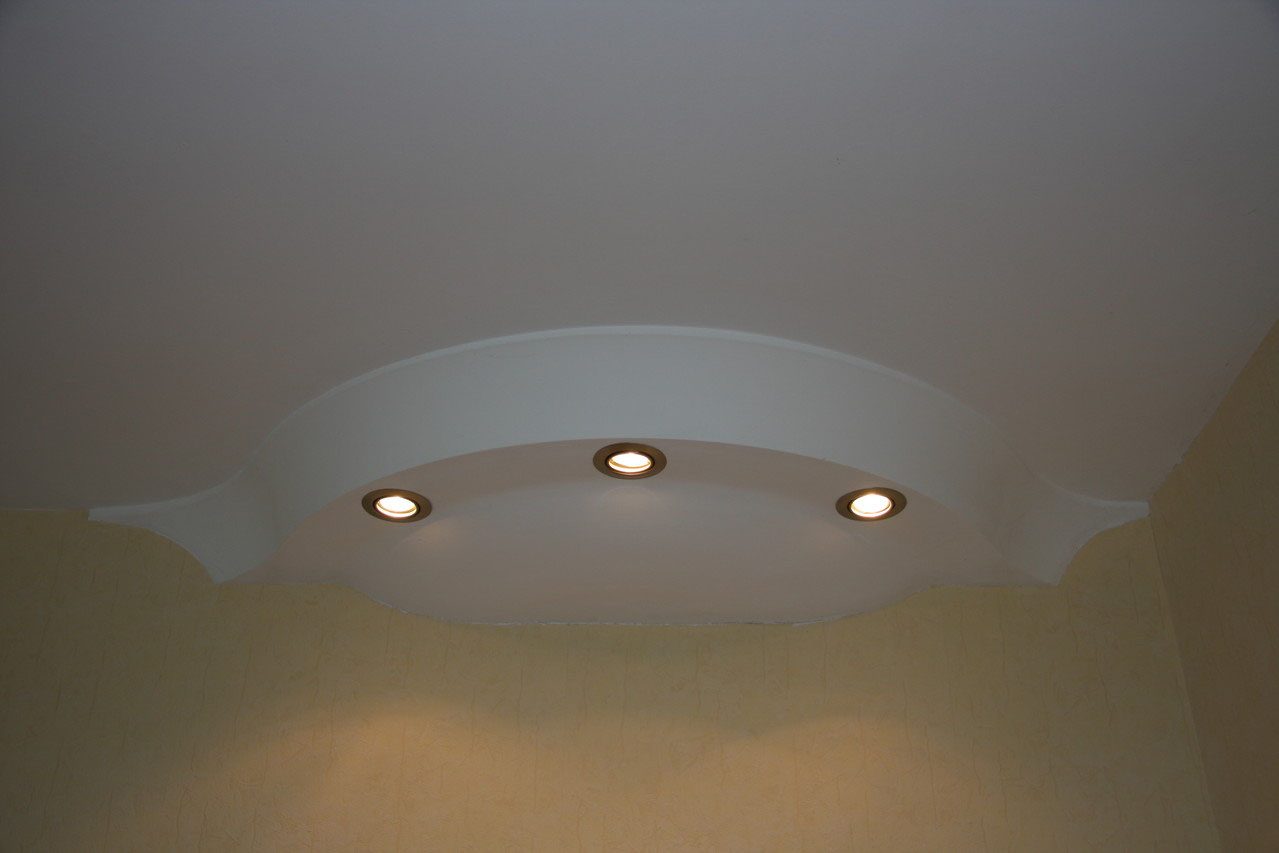 Geschwungene Lichtvoute mit drei Spots über einer gelben Wand